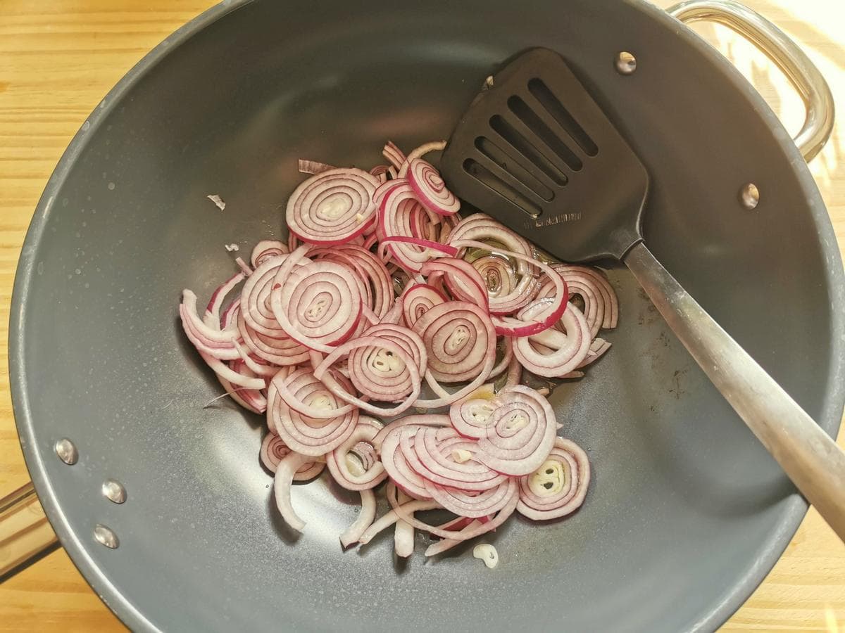 Sliced red onion cooking in deep skillet.