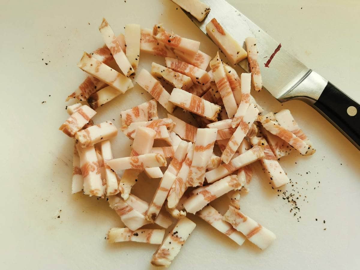 Guanciale cut into lardons on white chopping board.