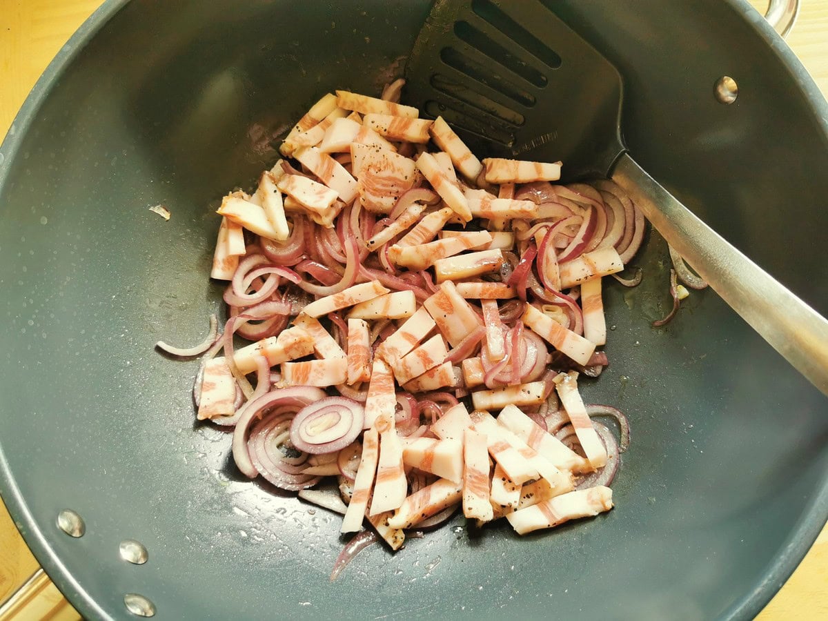 Guanciale lardons added to red onion in large skillet.