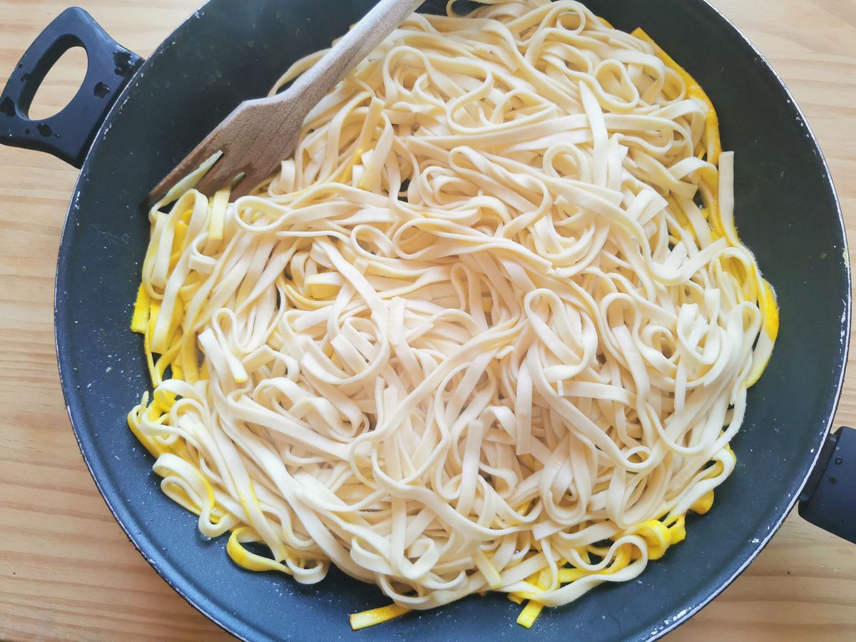 Cooked tagliolini added to skillet with saffron, lemon and butter sauce.