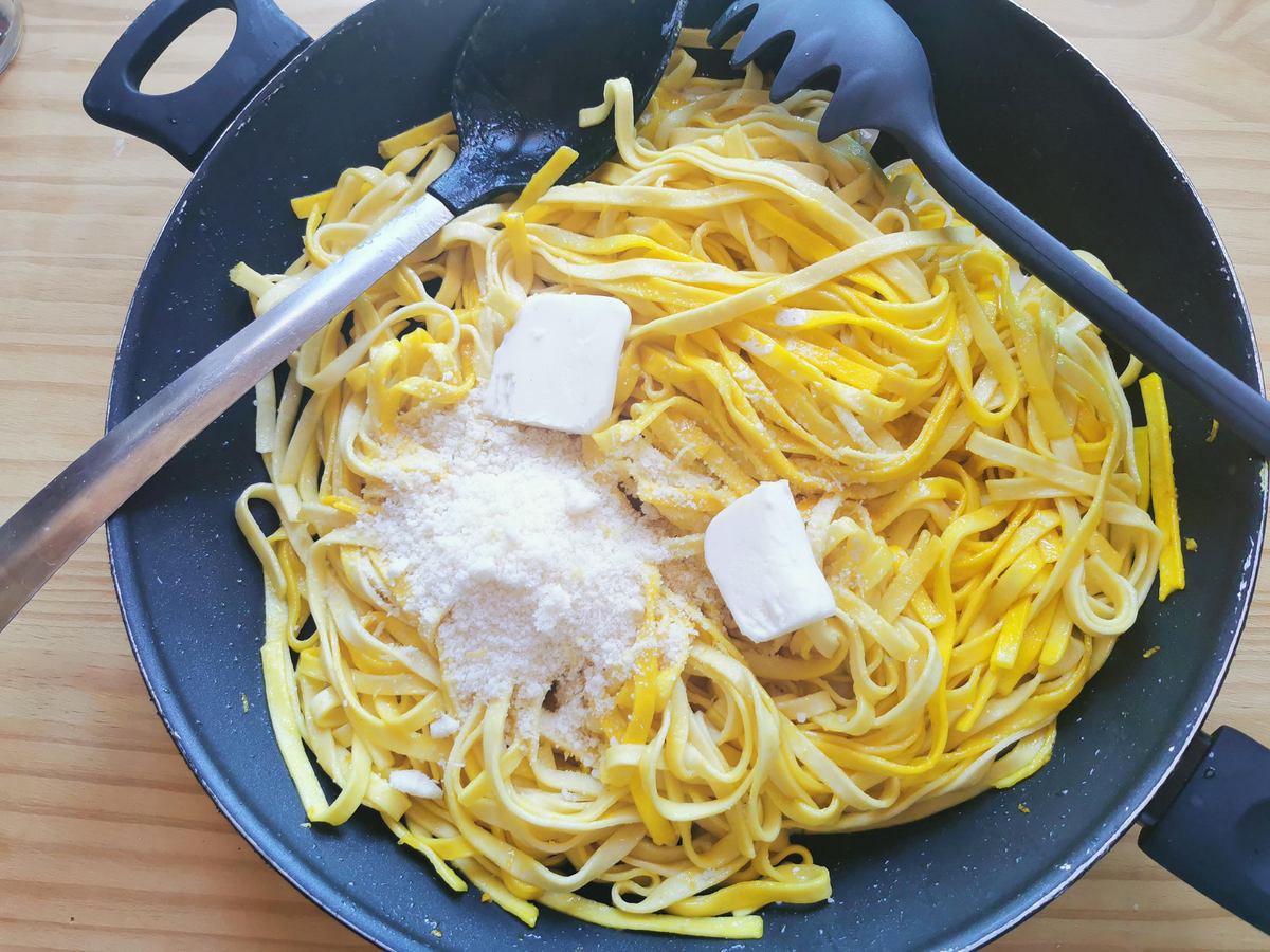 Cooked tagliolini mixed with saffron sauce in skillet with pieces of butter and grated Parmigiano on top.