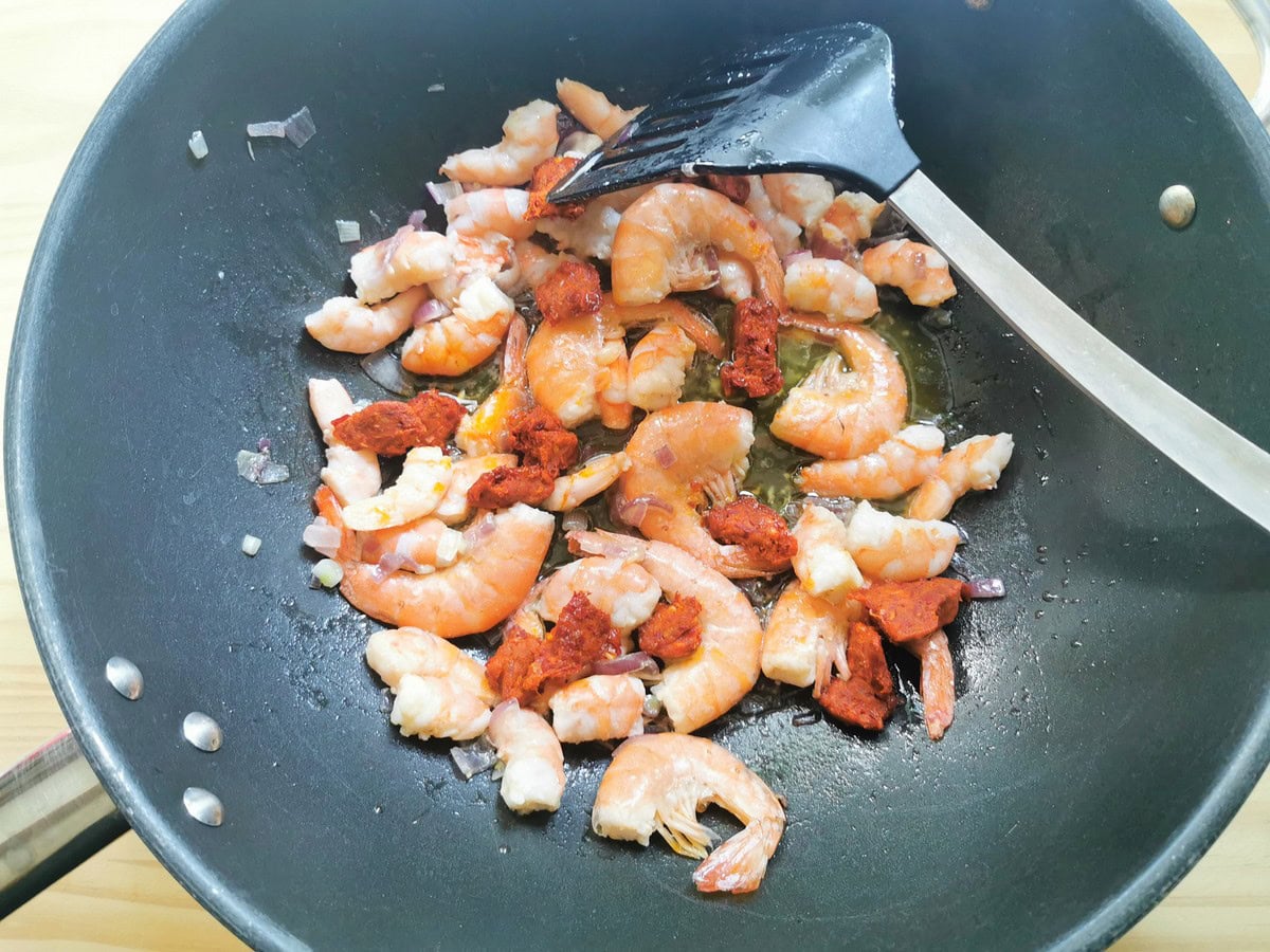 Chunks of nduja sausage added to shrimp and onion in skillet.