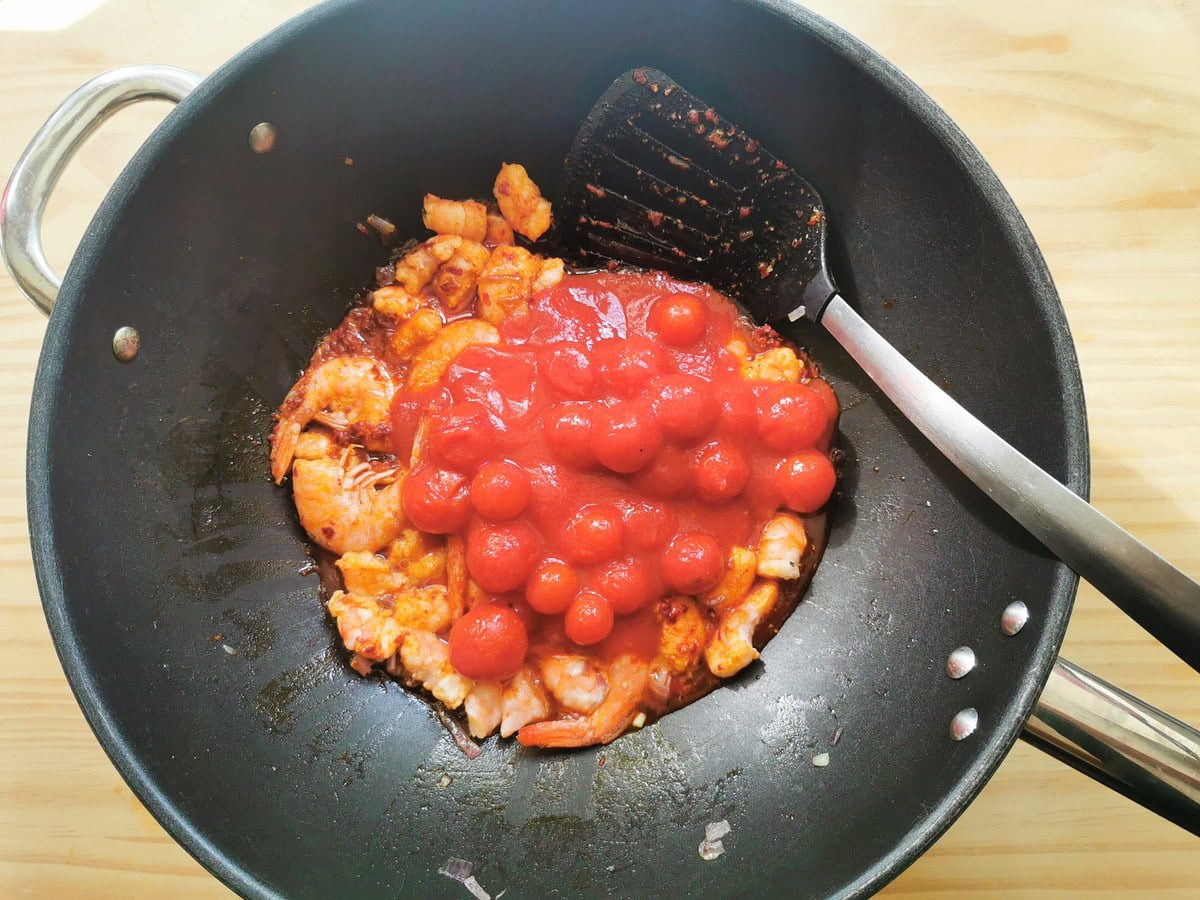 Canned cherry tomatoes added to shrimp and nduja in skillet.