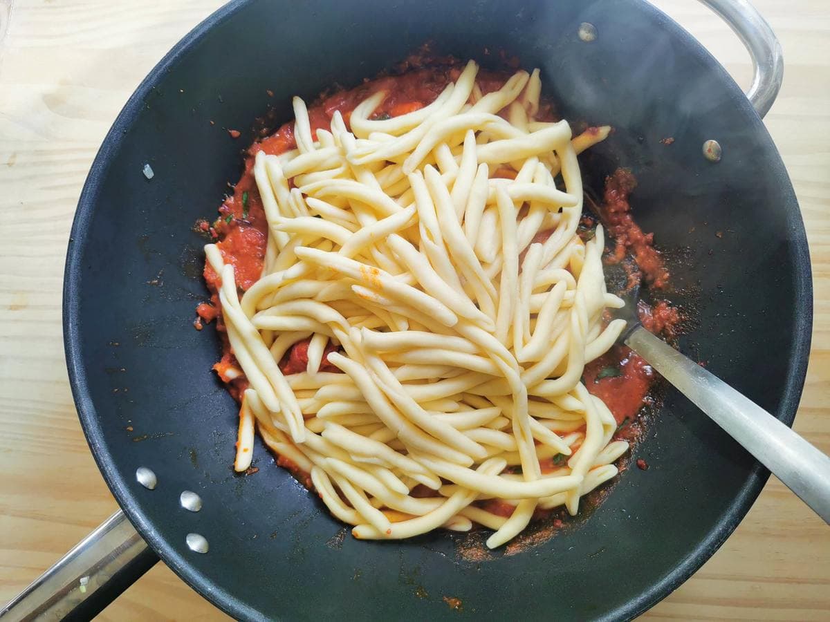 Cooked fileja pasta added to nduja and shrimp sauce in skillet.