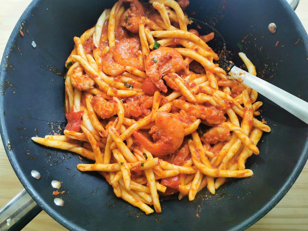 Cooked fileja pasta mixed with nduja and shrimp sauce in skillet.