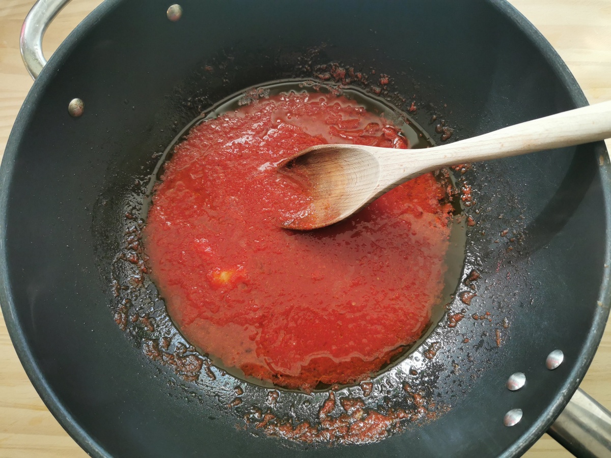 Tomato passata and garlic cloves cooking in large skillet.