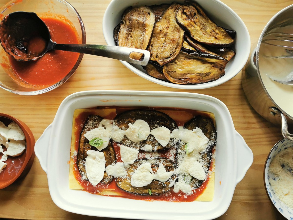 Lasagna sheets in rectangular oven dish with some tomato sauce, a layer of eggplant slices, some pieces of mozzarella, basil leaves, grated cheese and a couple of tablespoons of béchamel on top.