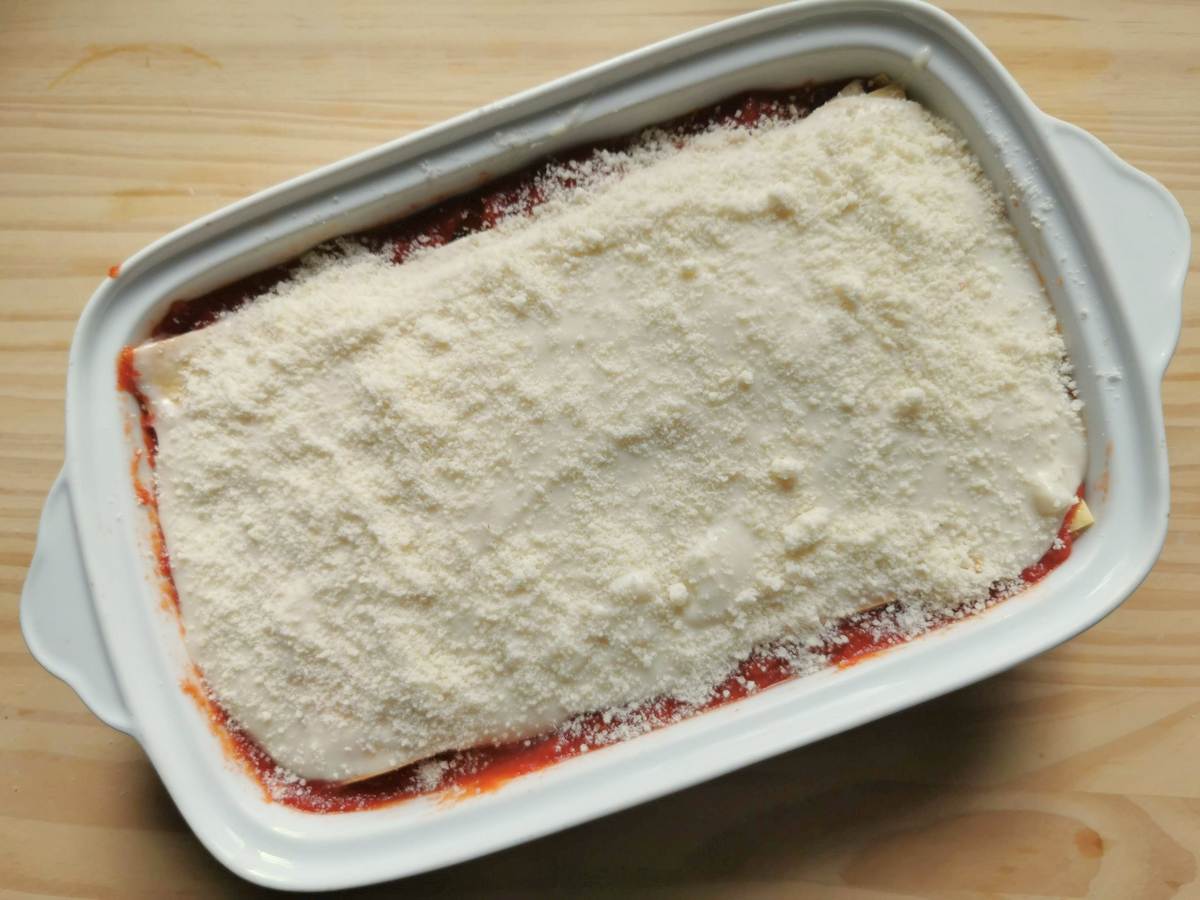 Eggplant parmigiana lasagna with final layer of bèchamel and grated cheese ready to go in the oven.