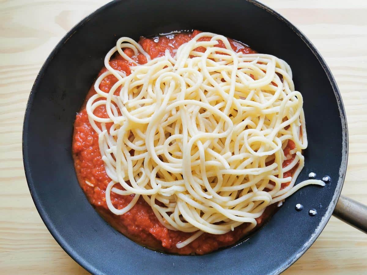 Cooked pici pasta in skillet with aglione sauce.