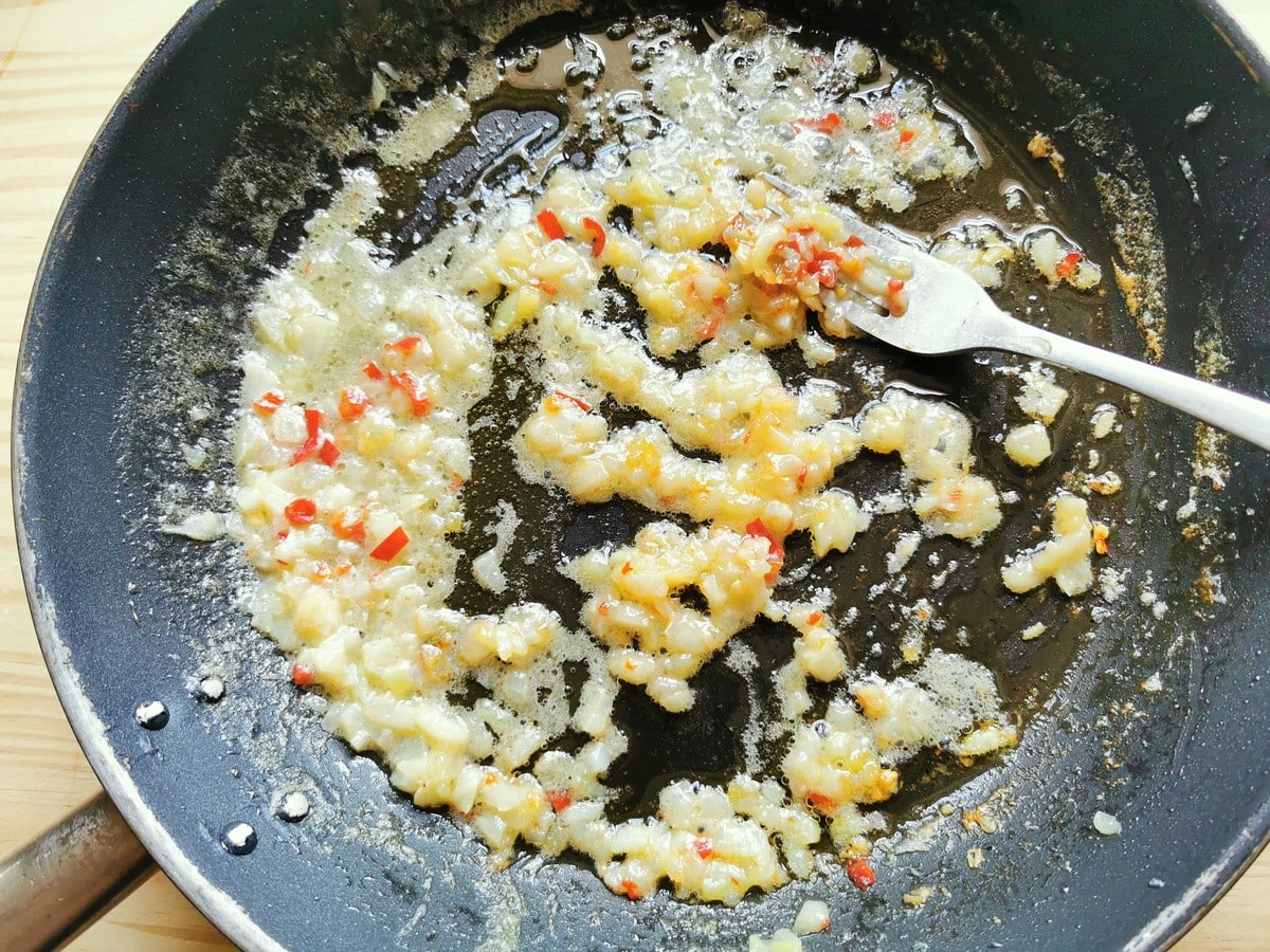Chopped aglione (elephant garlic) and peperoncino cooking in skillet in some water.