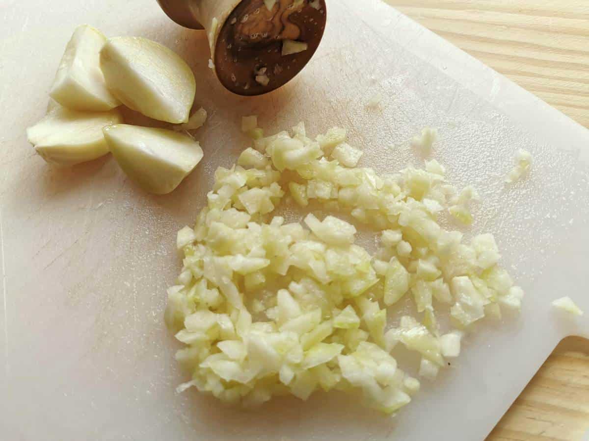 Peeled and chopped aglione (elephant garlic) cloves on white chopping board.