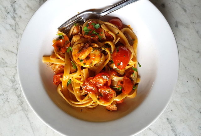 Fettuccine pasta with giant prawns and cherry tomatoes in white bowl