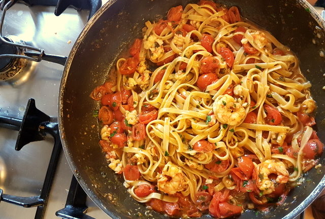 Fettuccine pasta with giant prawns and cherry tomatoes in frying pan