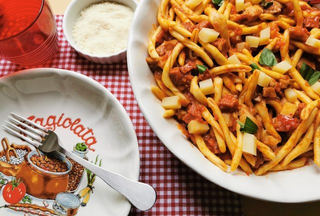 bowl of fileja alla Silana on table with empty white plate, fork and red glass