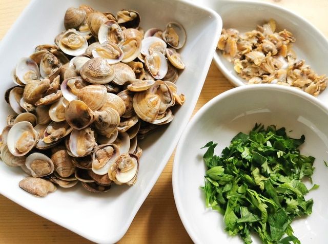 separated clams in a white bowl and chopped parsley in a white bowl
