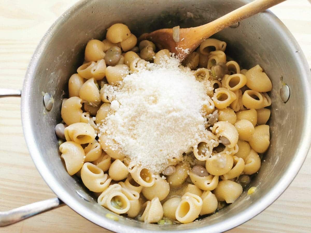 Cooked pasta and fava beans in pot with grated pecorino on top