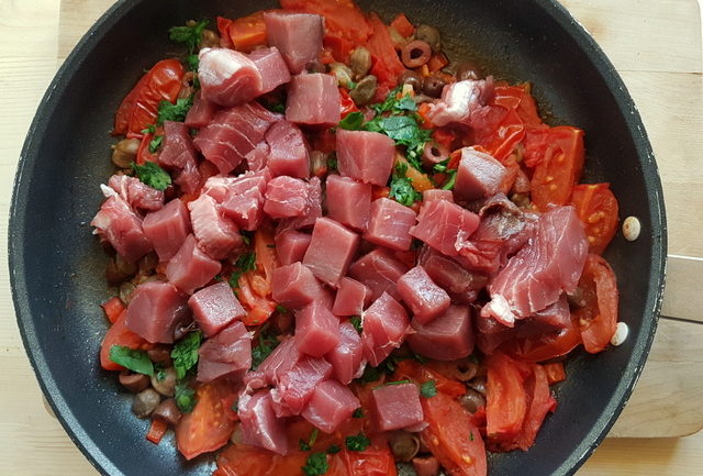 Fresh tuna chunks, tomatoes, olives, capers and parsley in frying pan