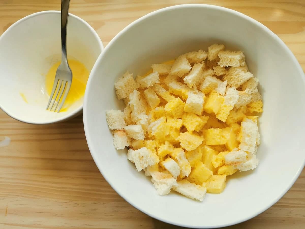 Stale bread cubes with milk and egg mixture in white bowl.