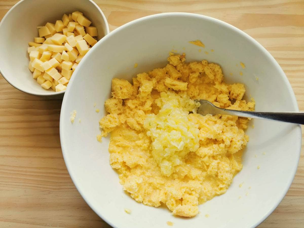 Fried onion in white bowl on top of bread cubes mixed with egg and milk.