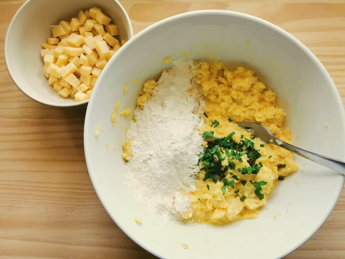 Flour and chopped chives and parsley in white bowl with bread, egg, onion and milk mixture.