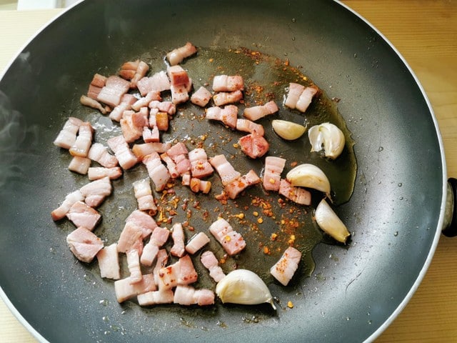 pancetta cubes, peperoncino flakes and garlic cooking in skillet