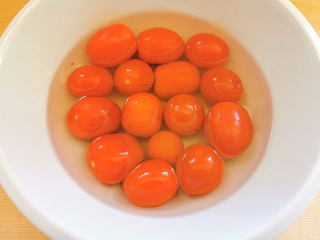 plum tomatoes in white bowl full of boiling water