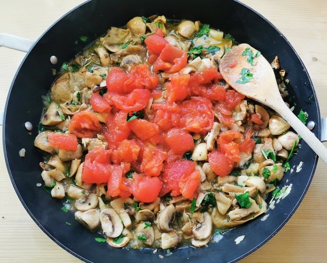 Chopped and peeled tomatoes with cooked mushrooms in skillet
