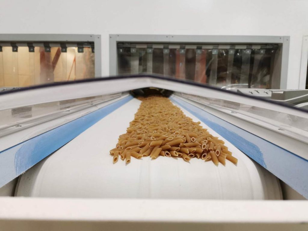 organic whole wheat penne pasta coming out of pasta making machine in pasta factory