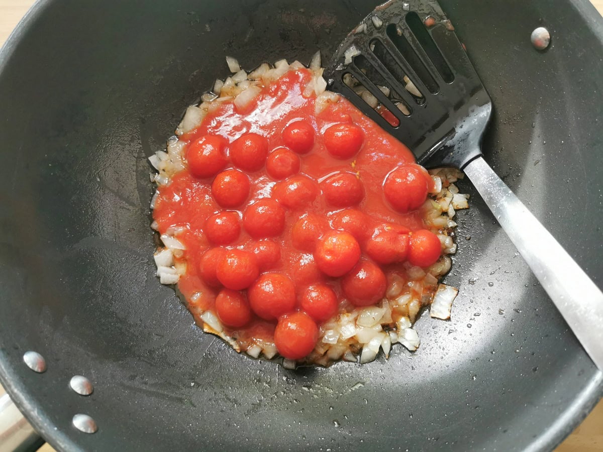 Canned peeled cherry tomatoes added to onion in large skillet.