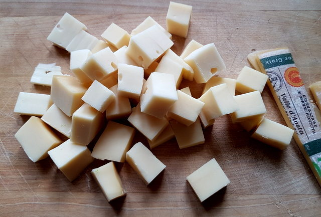 Fontina cheese cut into pieces on wooden board