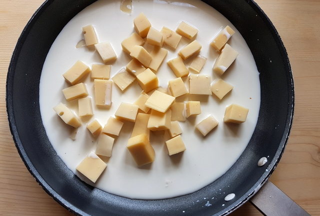 Fontina cheese pieces in skillet with milk and cream