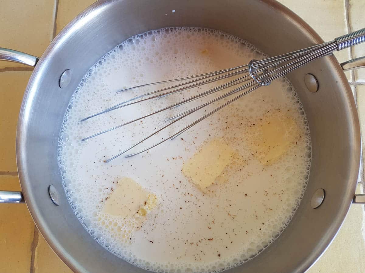 Milch, Butter, Salz und Muskatnuss in einem Topf mit einem Schneebesen verrühren