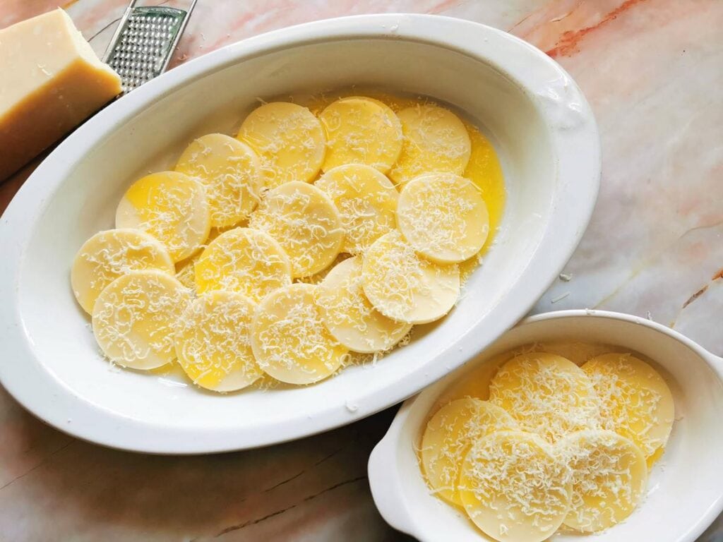 uncooked gnocchi alla romana in 2 oven dishes with melted butter and grated cheese on top
