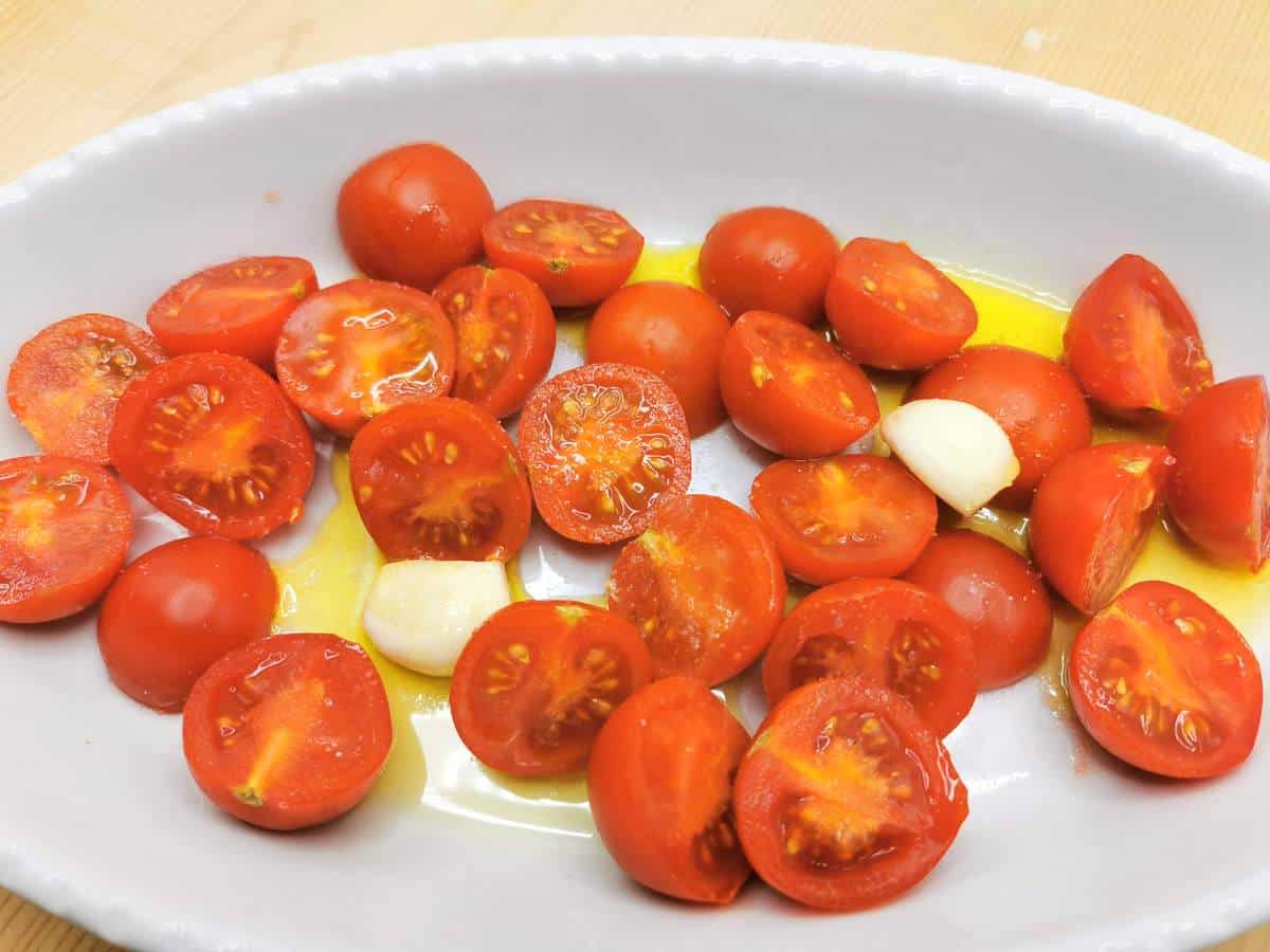 Cherry tomato halves with olive oil and garlic in oven dish.