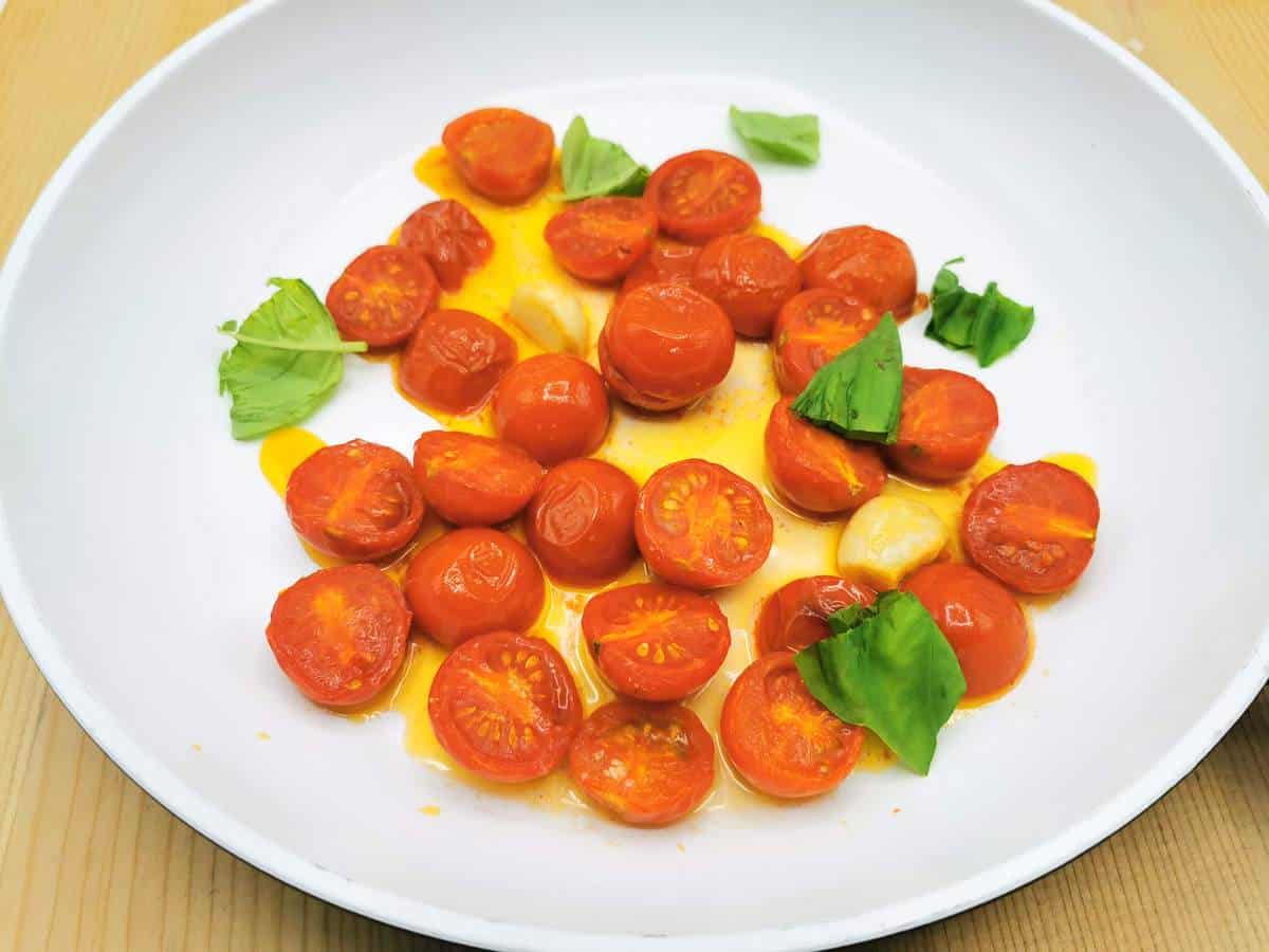Roasted cherry tomatoes in pan with basil and roasted garlic.