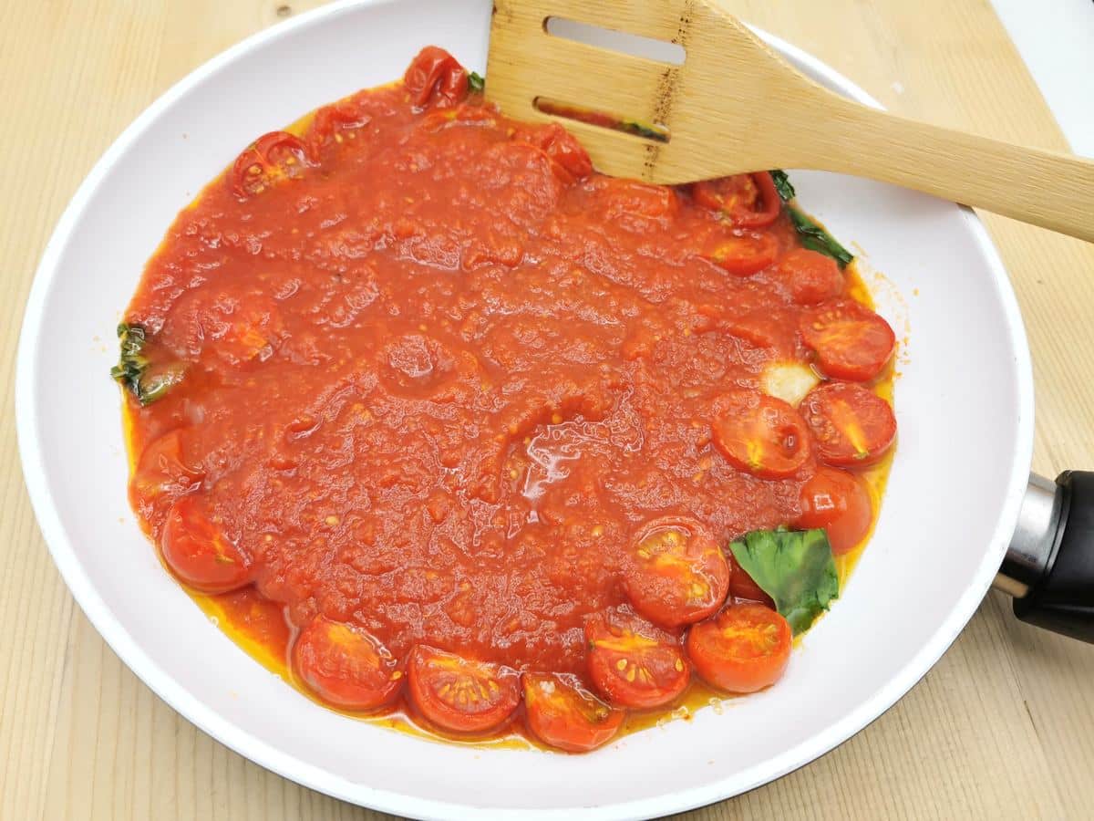 Tomato passata added to cherry tomatoes in pan.