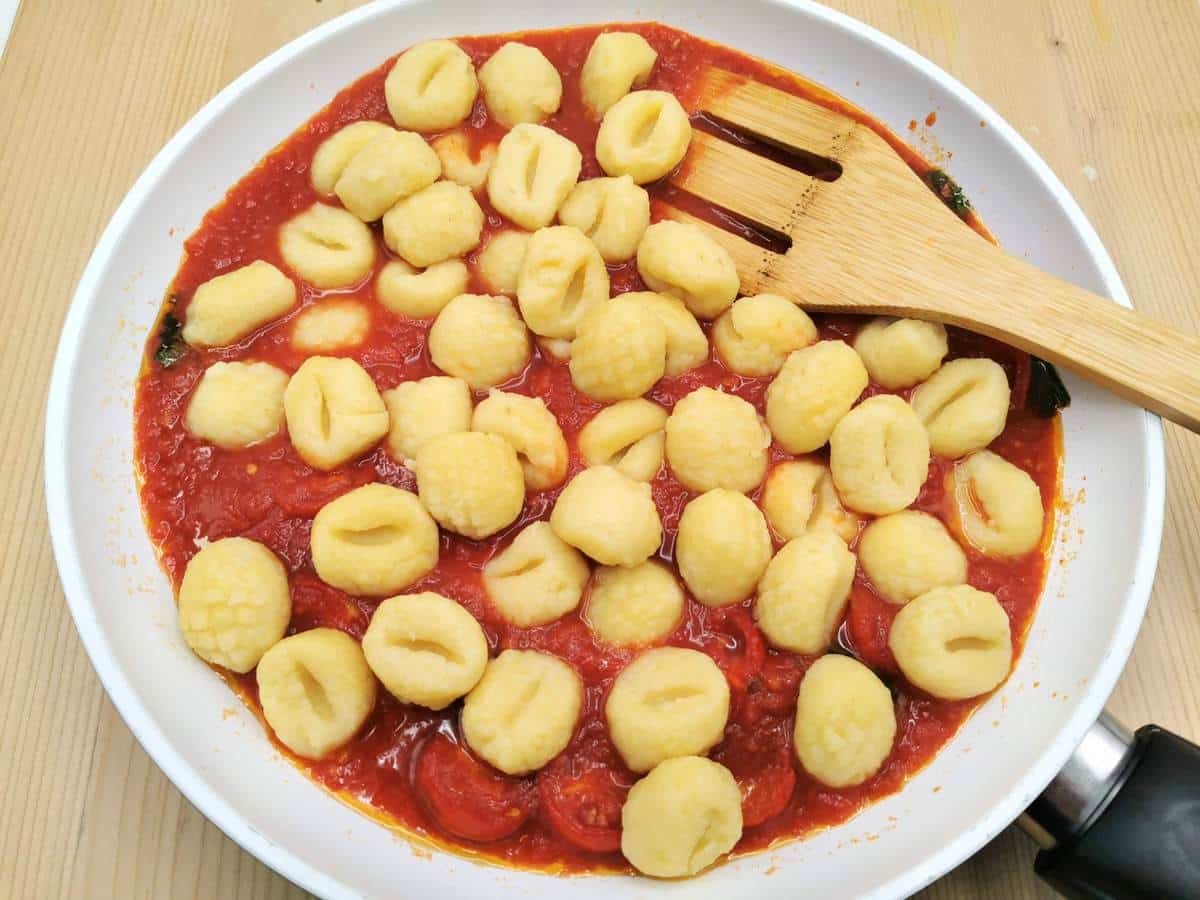 Cooked gnocchi added to tomato sauce in pan.