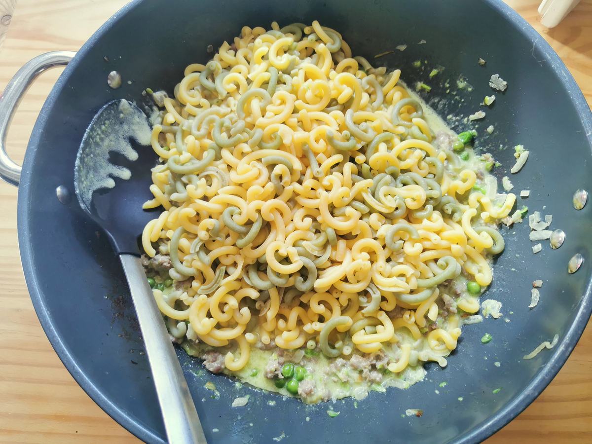 Cooked gramigna pasta in skillet with sausage, cream and peas.