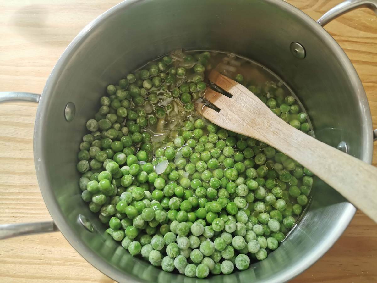Peas cooking in saucepan with onions and vegetable broth.