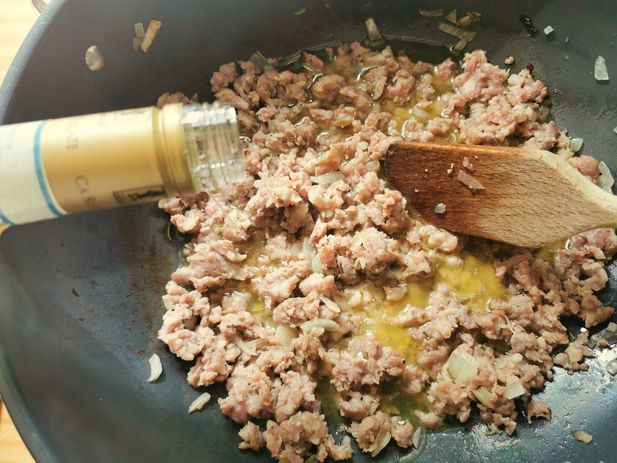 White wine being added to sausage and onion cooking in skillet.