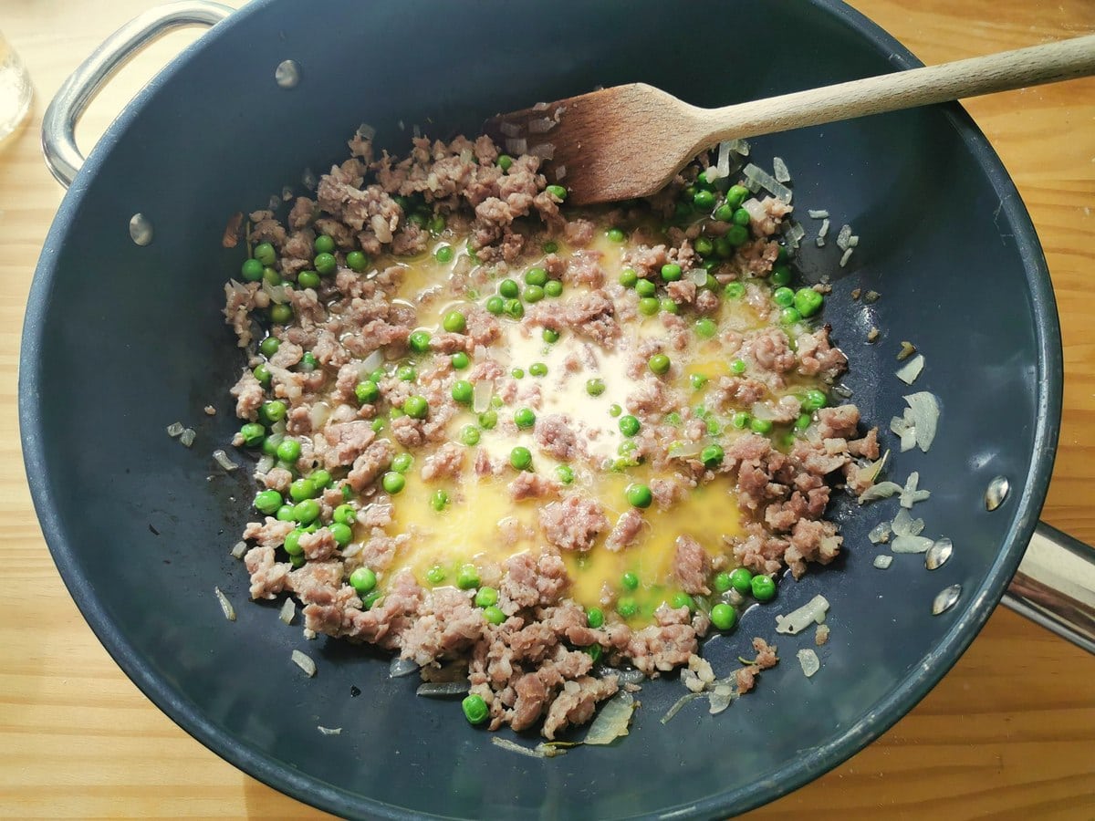 Fresh cream added to sausages and peas cooking in skillet.