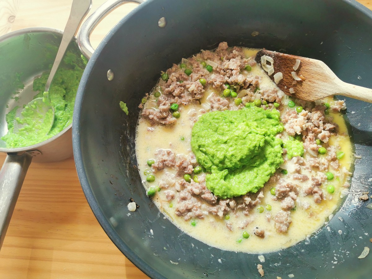 Pea purée added to sausage and cream sauce in skillet.