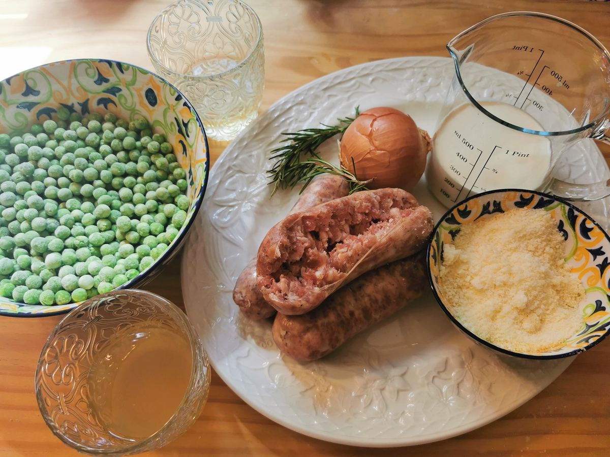 Ingredients for gramigna pasta with Italian sausage, cream and peas on white oval plate.