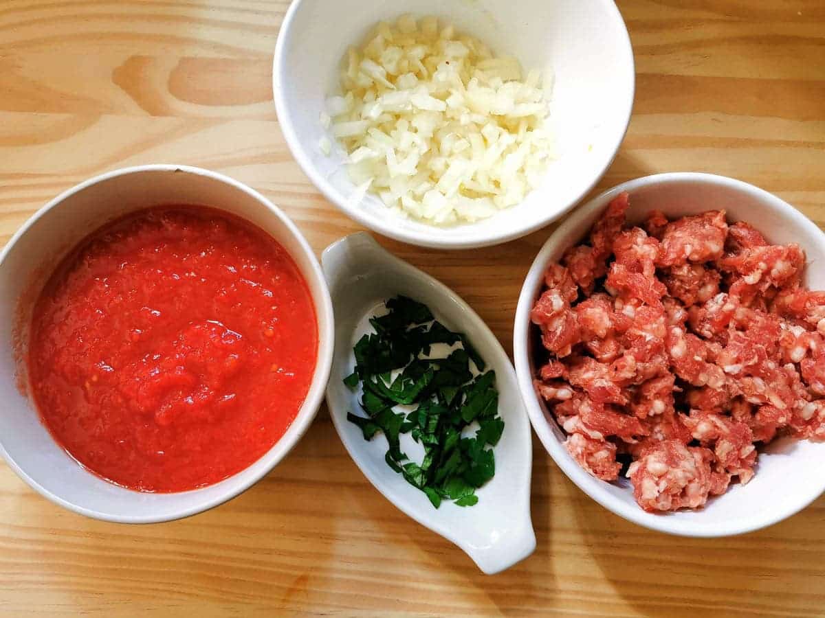 Minced sausage, chopped parsley, diced onions and canned tomatoes in separate bowls