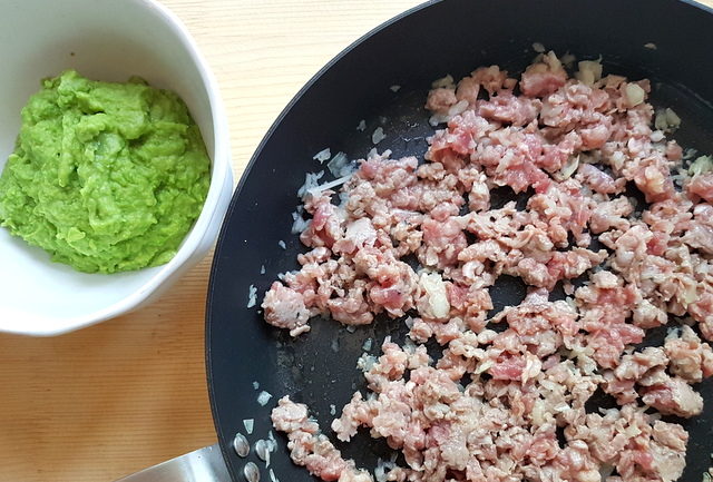 crumbled sausage meat and sliced onions in skillet next to pea puree in white bowl.