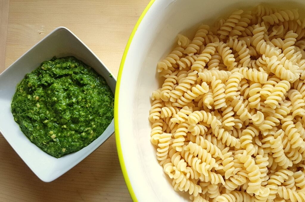 cooked pasta in large bowl and ready pesto in small white bowl