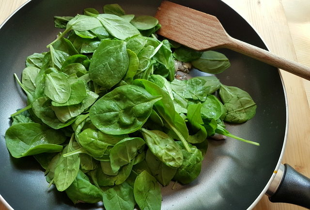 baby spinach leaves in frying pan with chopped shallots