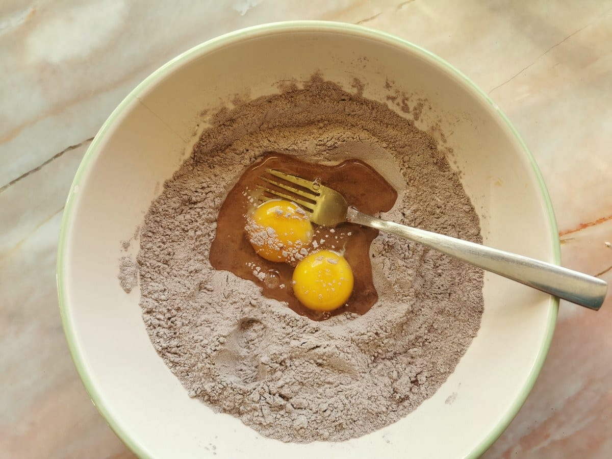 Two eggs broken into bowl with flour and cocoa powder.