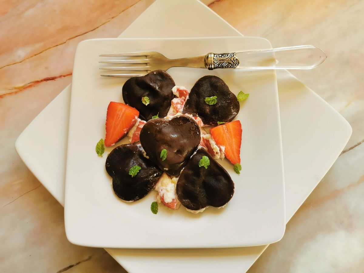 Heart-shaped chocolate ravioli on white plate with mascarpone and strawberry sauce.