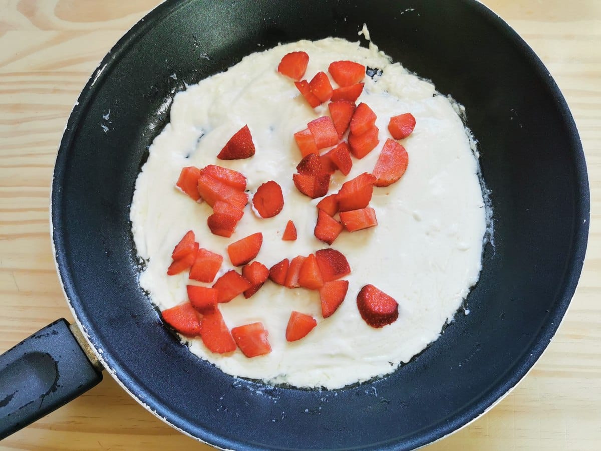Melted butter and mascarpone in frying pan with small pieces of strawberries in it.